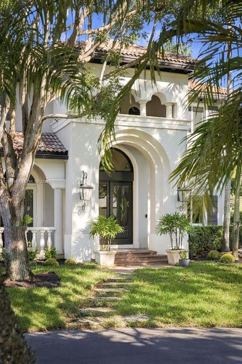 Stucco exterior featuring a prominent arched entryway, clay tile roof, decorative upper-level balustrade, and stone-finished steps