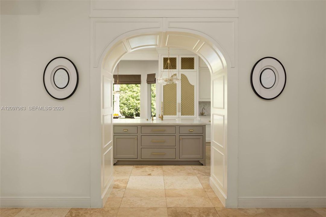 Arched entryway featuring intricate millwork, tile flooring, central kitchen island with drawers, and built-in cabinetry with decorative lattice-style detailing
