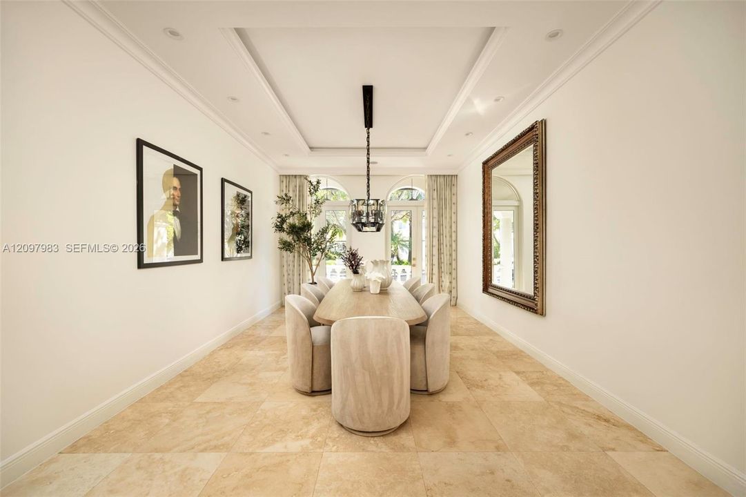 Tray ceiling with recessed lighting, large-format stone tile flooring, and arched glass-paneled doors with ornamental wrought iron accents