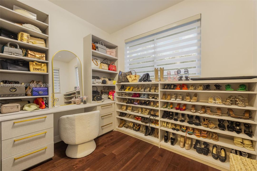 Custom built-in cabinetry featuring extensive open shelving, integrated vanity station with drawer storage, gold-finish hardware, and wood-finish flooring