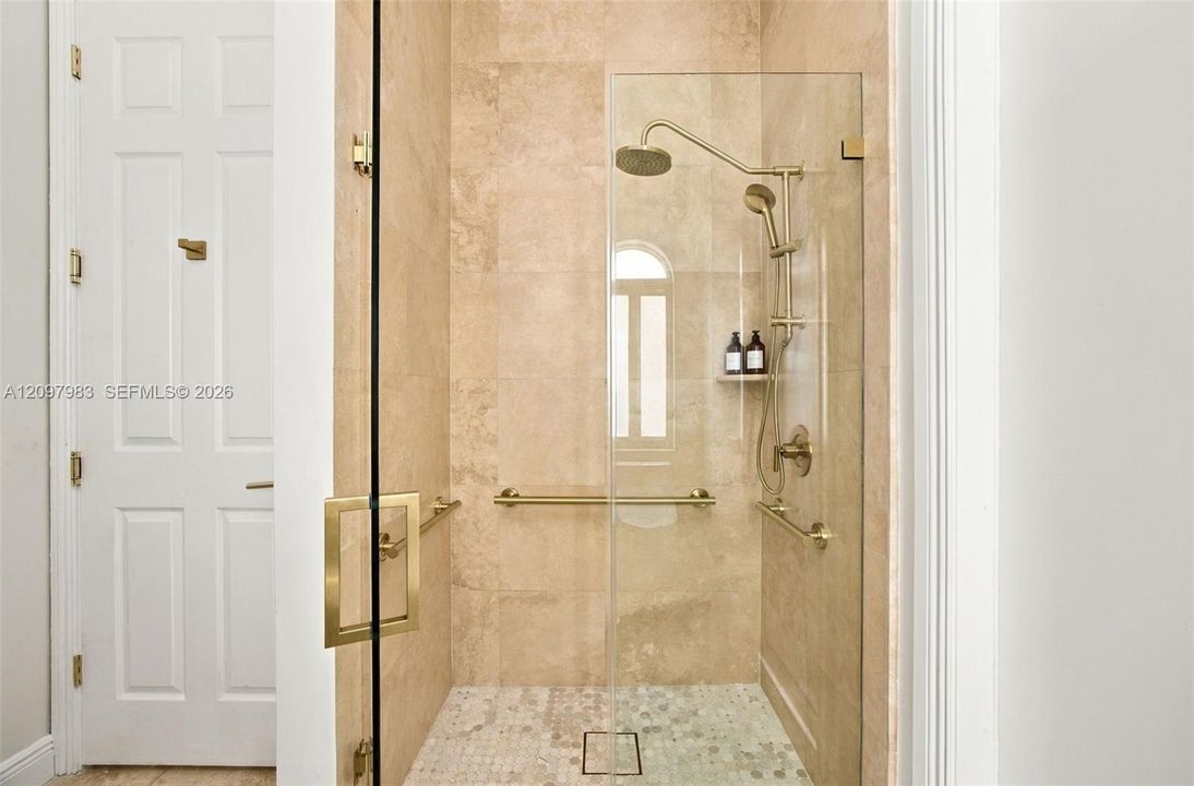 Walk-in shower featuring floor-to-ceiling stone tile, a glass enclosure, brass-finish fixtures, a dual-head shower system, and integrated brass-finish support bars