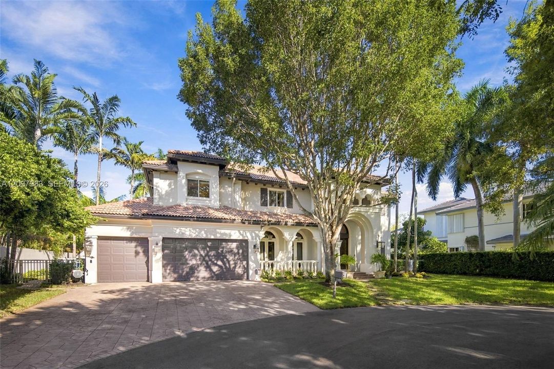 Two-story stucco exterior featuring a tiled roof, arched architectural detailing, a multi-car garage, and a paver driveway