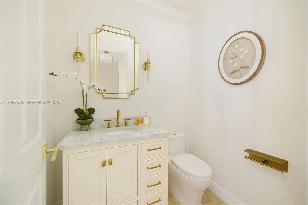 Custom cabinetry vanity with stone countertop, brass-finish fixtures, geometric wall mirror, and coordinating brass-finish hardware