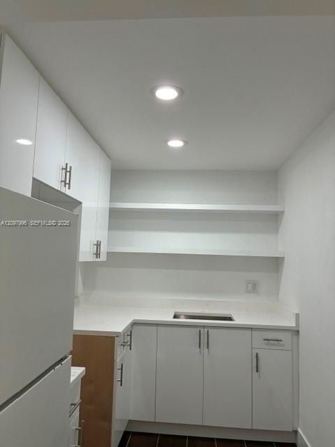 White cabinetry with stainless steel hardware, white stone-composite countertops, recessed ceiling lighting, and open wall shelving