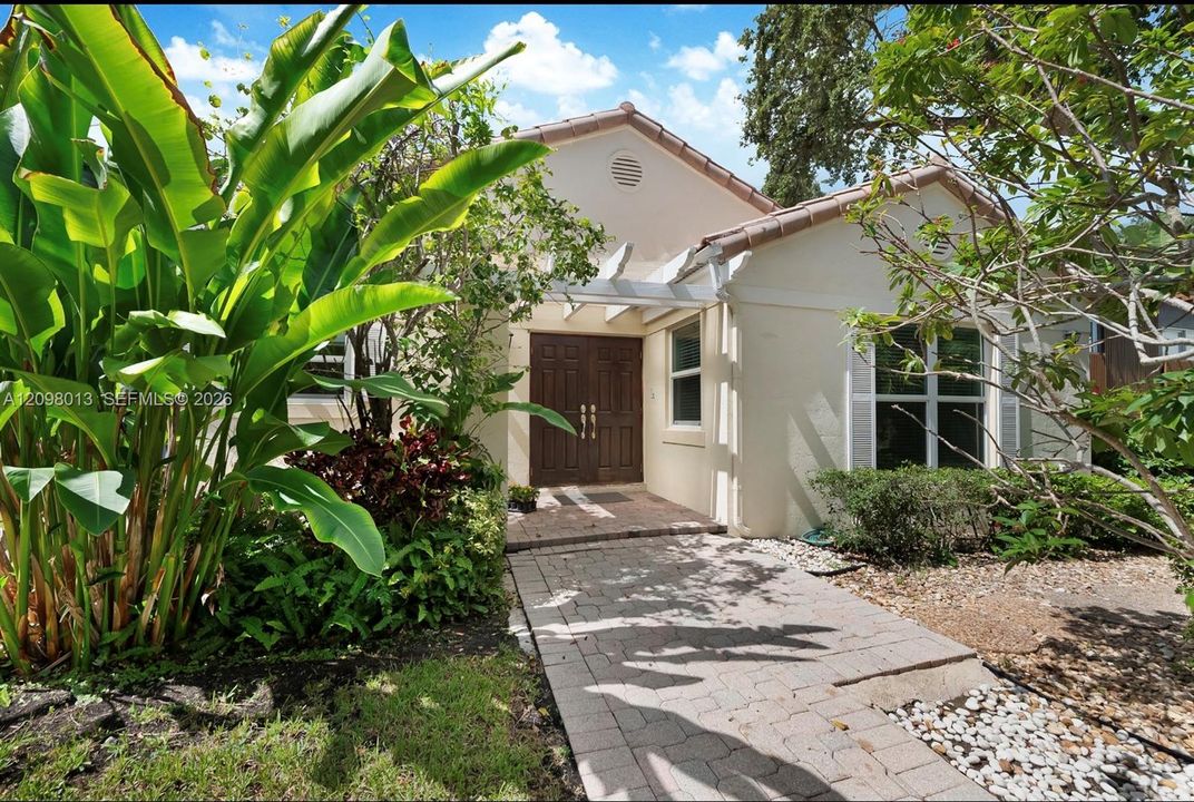 Stucco on concrete exterior featuring a tiled roof, paver stone walkway, double entry doors, and overhead trellis. Built on concrete slab no crawl space.