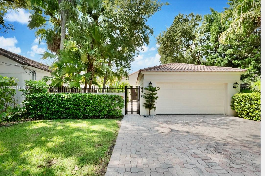 Exterior featuring a paved driveway, metal pedestrian gate, tiled roof, and perimeter wall with integrated greenery