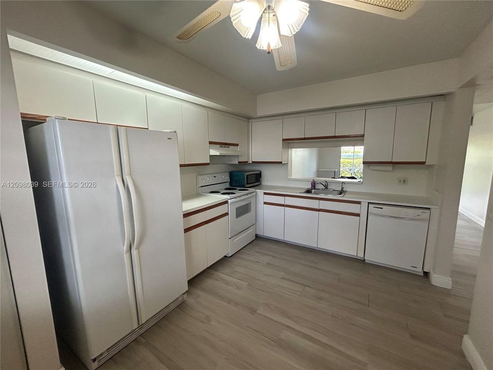Kitchen featuring white flat-panel cabinetry with wood trim, wood-finish flooring, solid-surface countertops, and built-in appliances