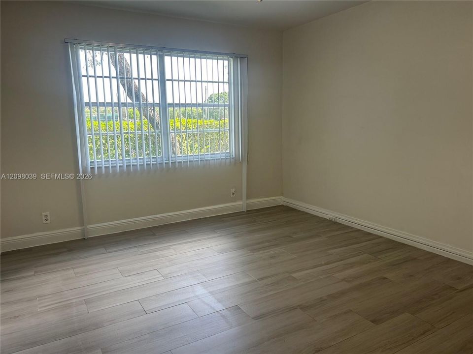 Interior space featuring wood-finish flooring, neutral wall paint, and a large window equipped with vertical blinds