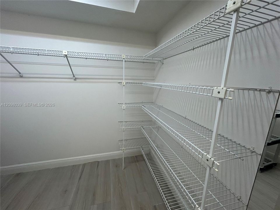 Storage space featuring tiered white wire shelving units and wood-finish tile flooring