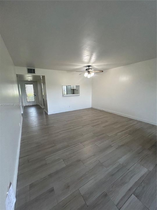Open-concept room featuring wood-finish flooring, a ceiling fan with multi-light fixture, and a rectangular wall cutout