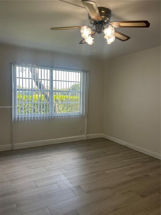 Wood-finish flooring, ceiling fan with integrated four-light fixture, and large window with vertical blinds