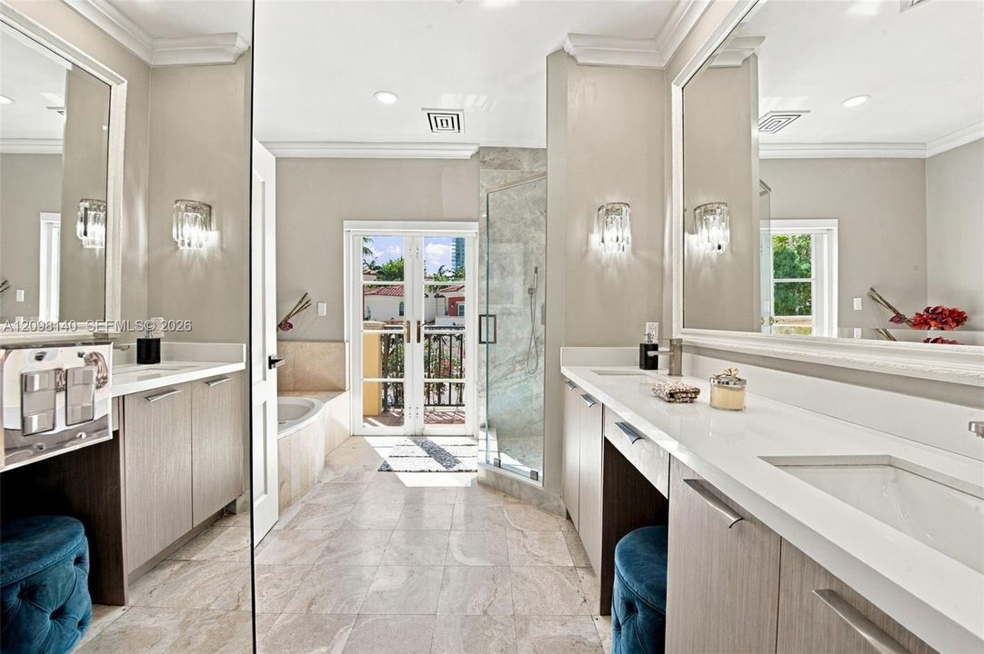 Bathroom featuring dual vanities with light wood-finish cabinetry, quartz countertops, a stone-surround soaking tub, glass-enclosed shower, and French doors