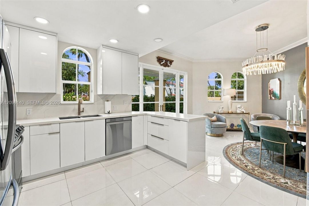 Modern kitchen featuring high-gloss white cabinetry, polished stone countertops, stainless steel appliances, arched windows, and large-format tile flooring