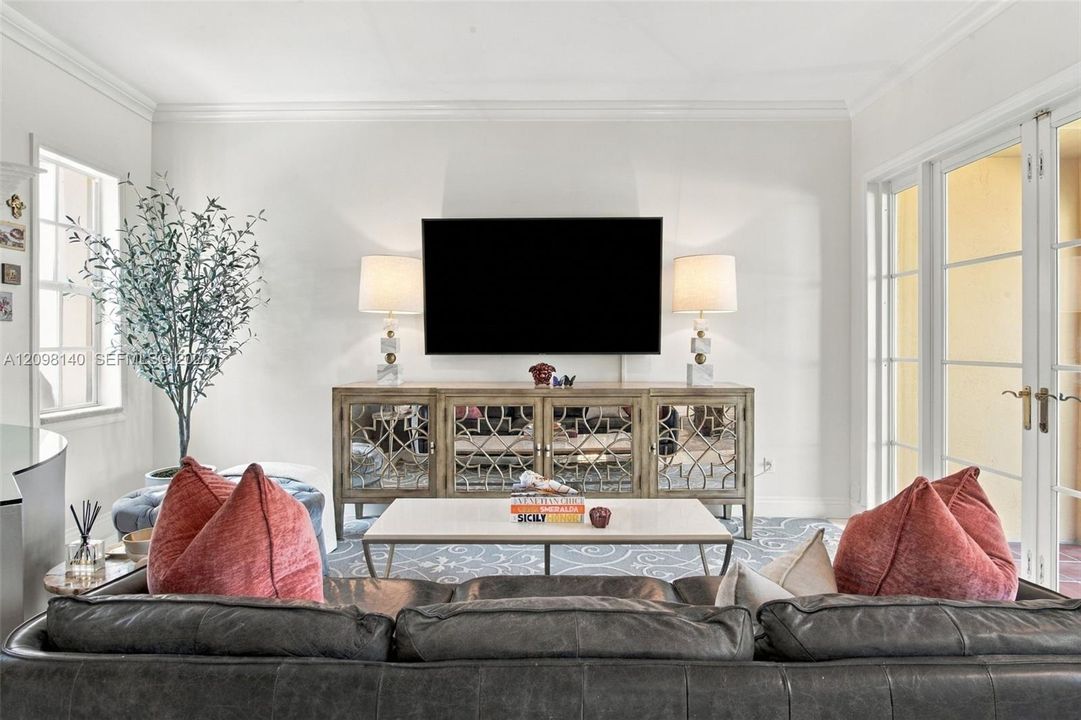 Living area featuring crown molding, multi-pane glass doors, and large windows with recessed framing
