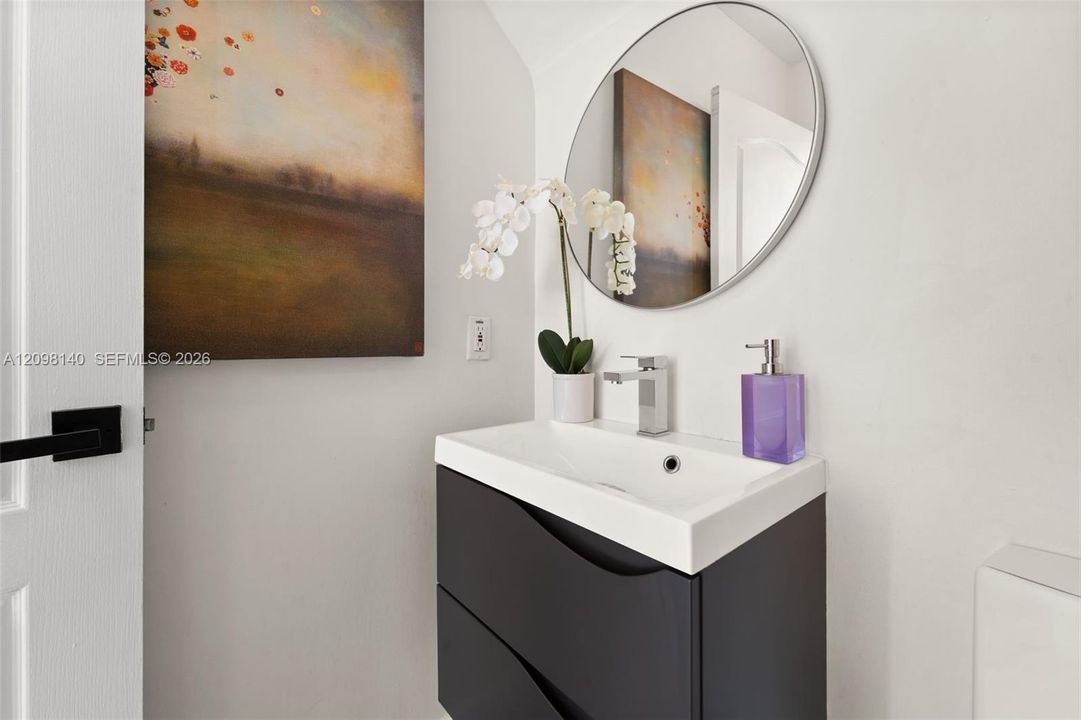 Modern wall-mounted dark cabinetry with a white integrated sink, polished chrome single-handle faucet, and circular frameless mirror