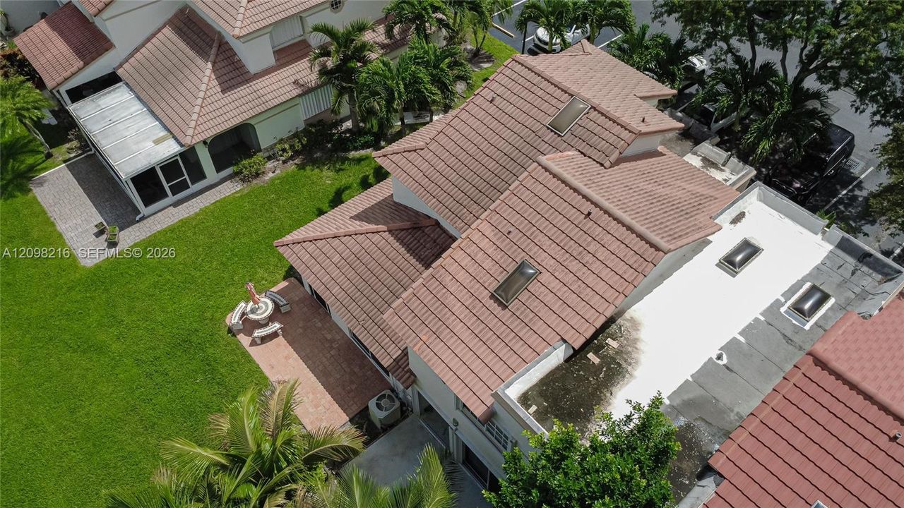 Aerial view of the home and its tile roof, surrounded by mature landscaping and green space.