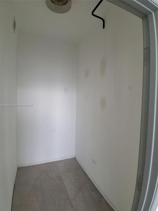 Enclosed space featuring grey tile flooring, ceiling-mounted light fixture, and a single wall-mounted hook