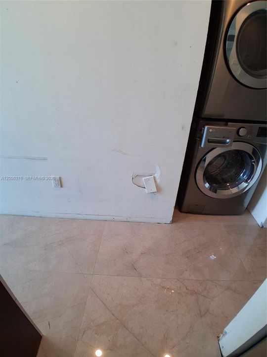 Stacked stainless steel laundry appliances set against polished stone flooring