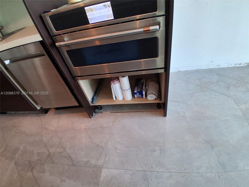 Stainless steel double wall oven, integrated dishwasher with panel-matching finish, dark wood-tone cabinetry, and large-format porcelain tile flooring