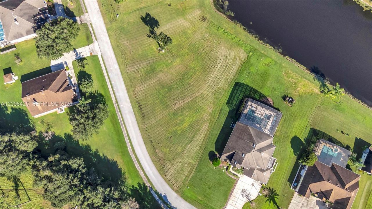Aerial perspective featuring a vacant residential lot, expansive lawn, mature trees, and water frontage