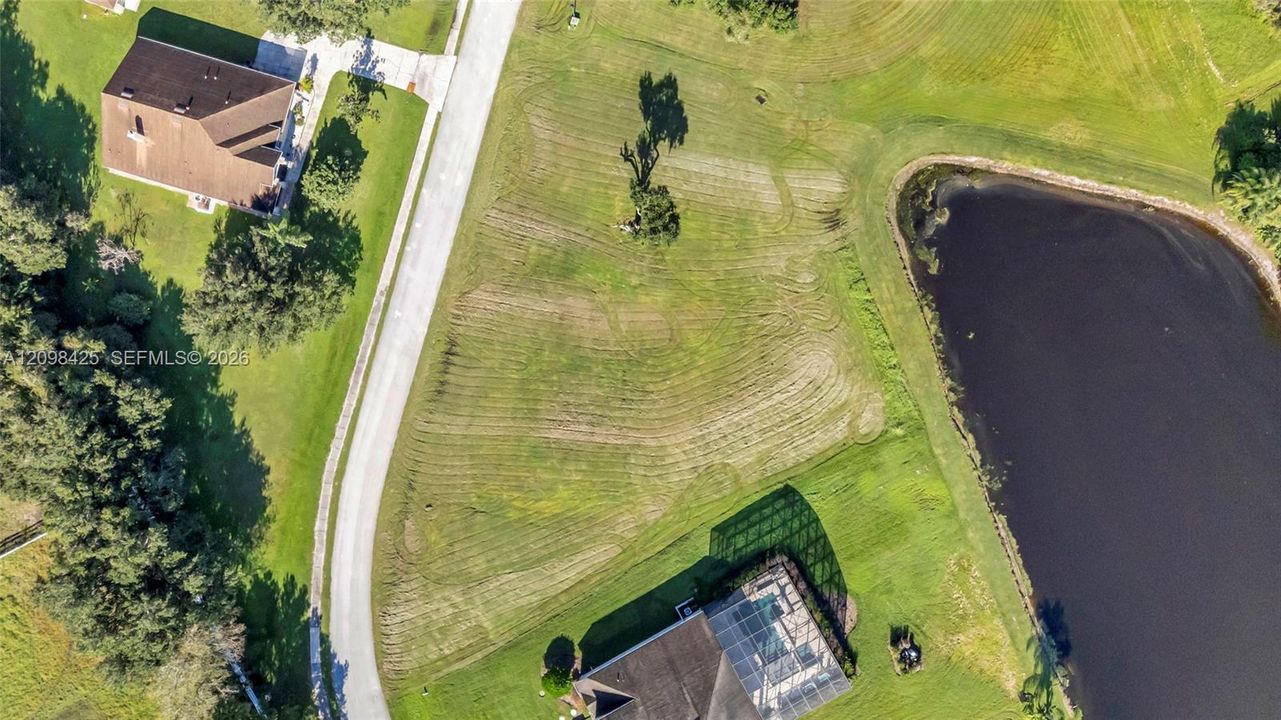 Aerial perspective of a vacant lot featuring a manicured lawn, paved road access, and waterfront positioning