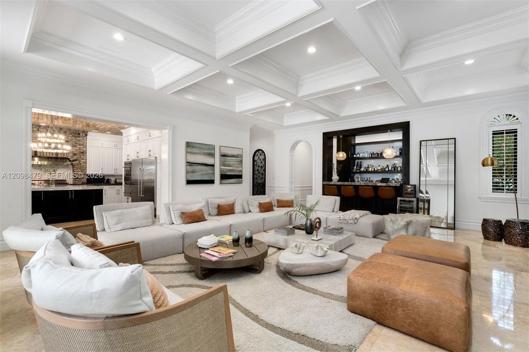 Coffered ceiling with recessed lighting, integrated wet bar, arched doorway, arched window with plantation shutters, and polished stone flooring