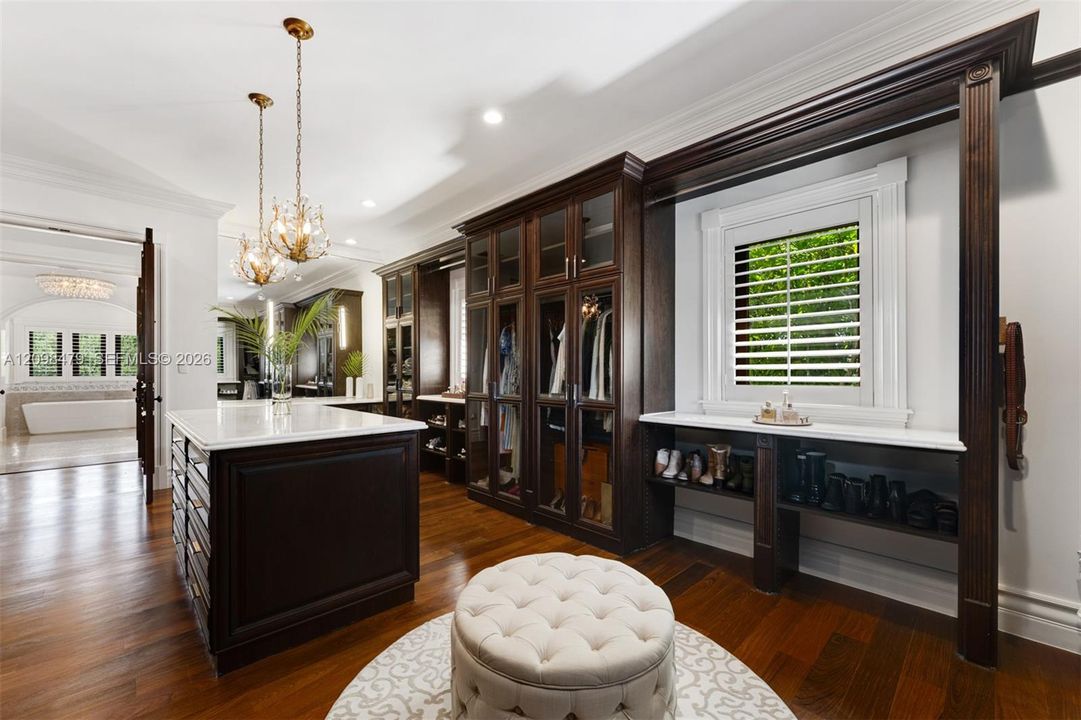 Dark wood-finish flooring with a central storage island, built-in glass-front cabinetry, and custom window shutters