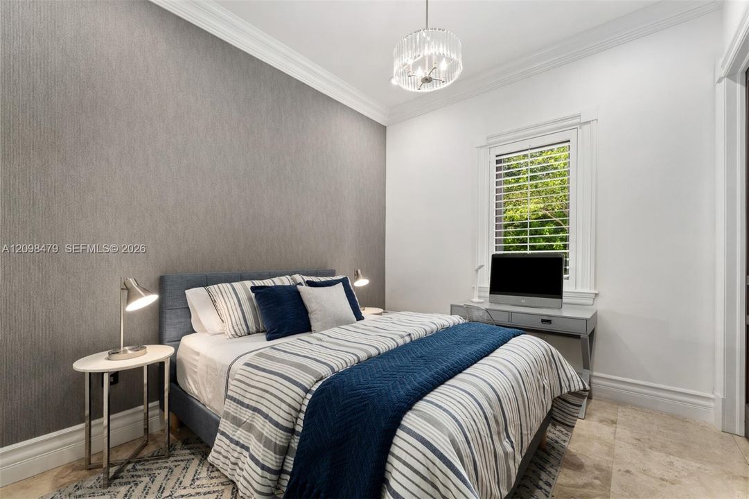 Textured accent wall, crown molding, crystal chandelier, plantation shutters, and light-toned tile flooring