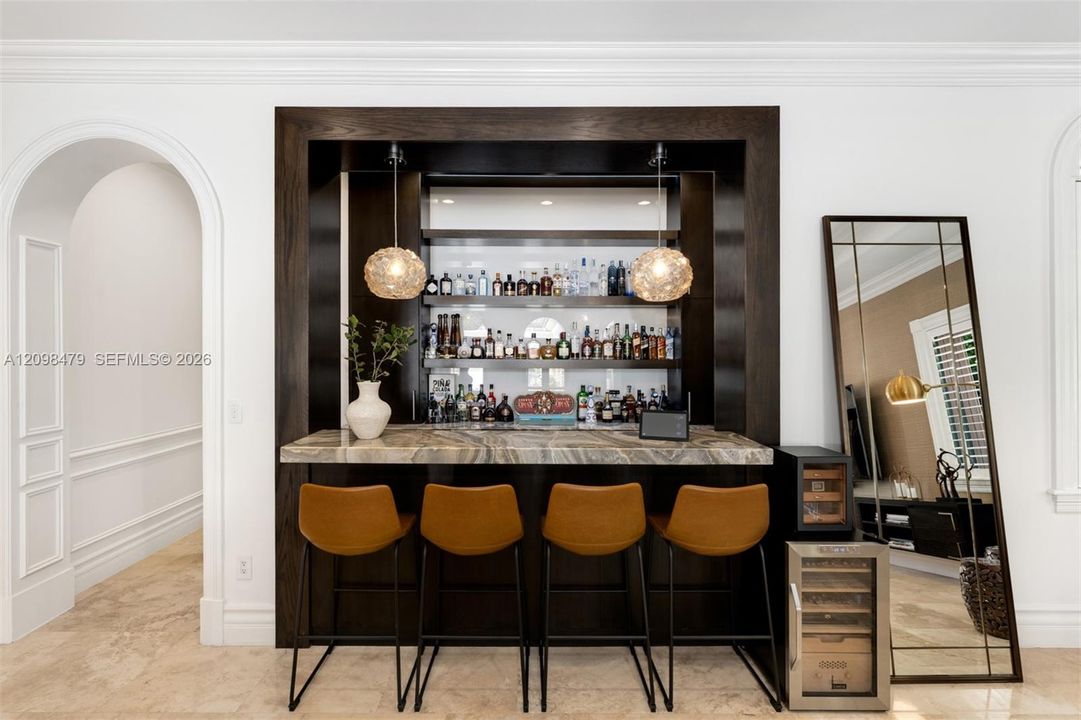 Built-in wet bar with a dark wood finish and stone countertop, illuminated by two pendant light fixtures