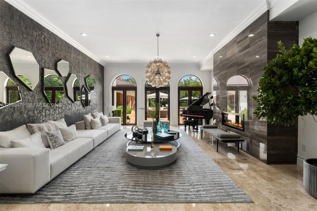 Recessed lighting, arched double doors, stone-finish flooring, accent wall with textured finish, and a dark stone fireplace with linear firebox
