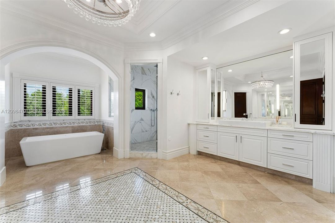 Freestanding soaking tub, walk-in shower with marble-finish walls, dual vanity with extensive storage, full-height wall mirror, and chandelier lighting