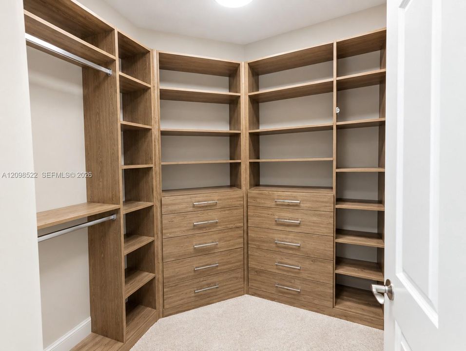 Walk-in closet featuring custom wood-finish built-in shelving, multiple integrated storage drawers, brushed metal hardware, and hanging rods