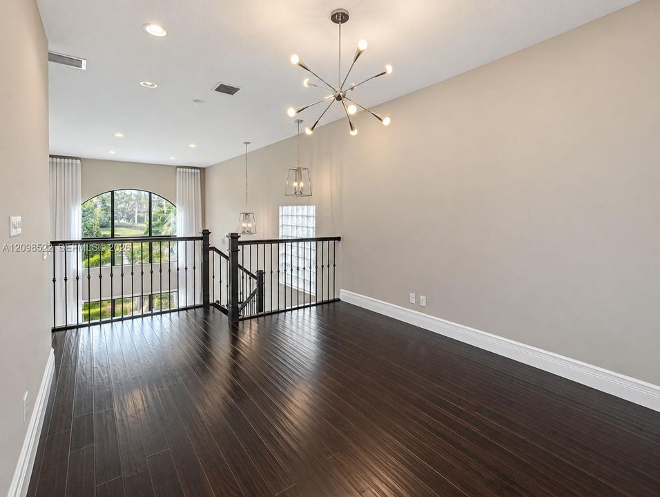 Open loft featuring dark wood-finish flooring, a modern sputnik-style chandelier, recessed lighting, and a wrought-iron staircase railing with an arched window