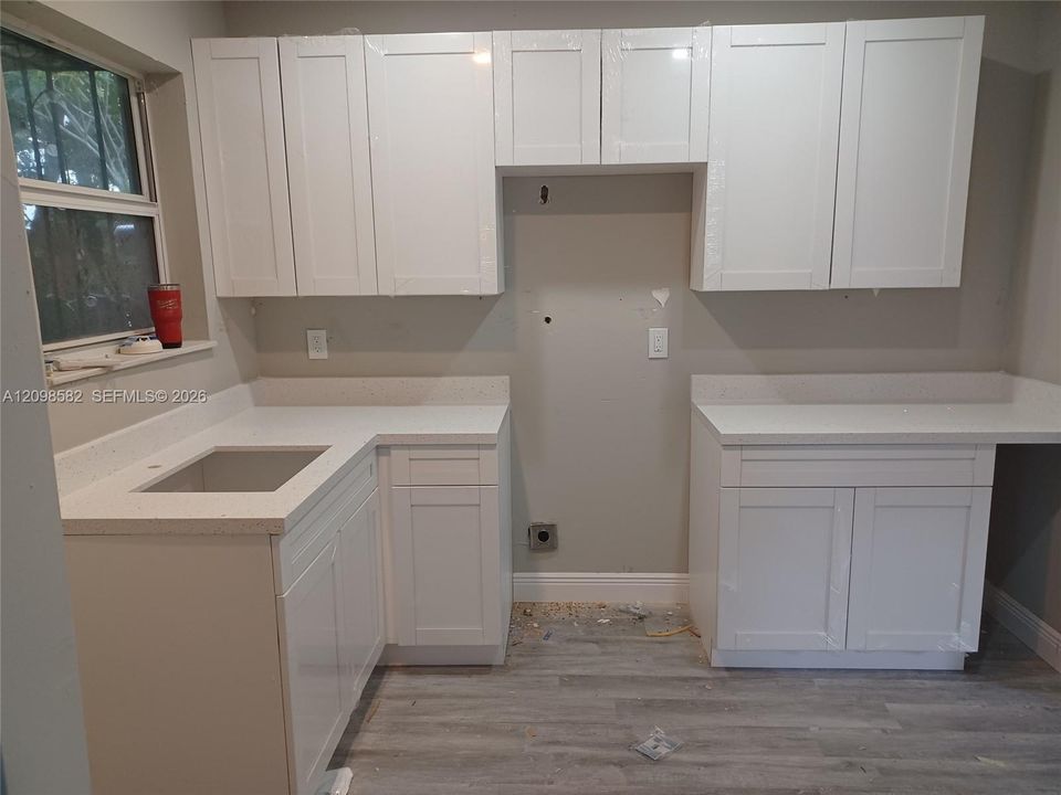 White shaker-style cabinetry with integrated hardware, neutral solid-surface countertops, undermount sink, and wood-finish flooring