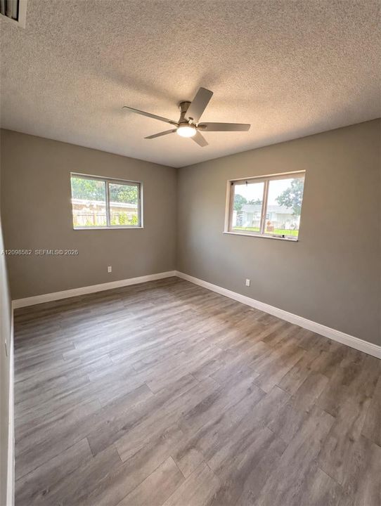 Neutral-toned interior featuring wood-finish flooring, dual windows with white frames, and a central ceiling fan with integrated lighting