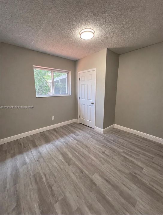 Room featuring wood-finish flooring, neutral wall paint, a six-panel door, and a flush-mount ceiling light fixture