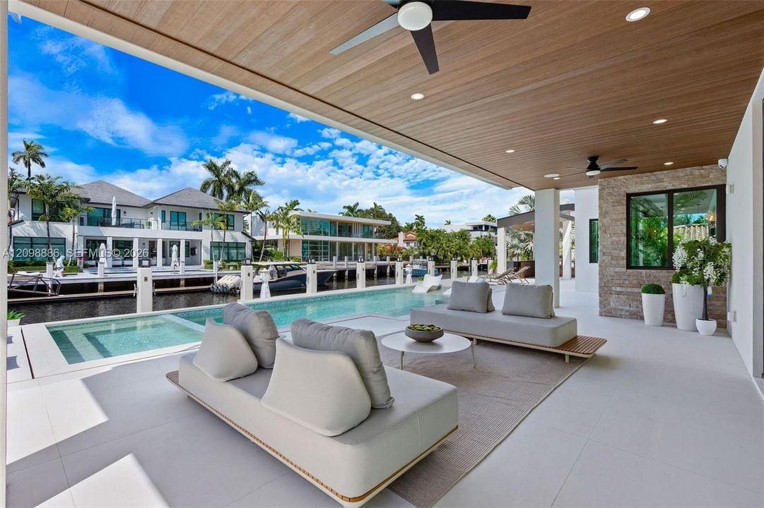 Covered patio featuring a wood-plank ceiling, recessed lighting, and dual ceiling fans, complete with a stone-accented wall and a custom pool bordering the canal