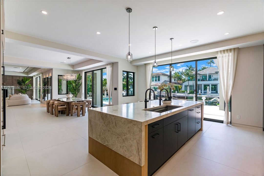 Kitchen featuring a large central island with waterfall-edge countertop, dark cabinetry, recessed lighting, and expansive sliding glass doors