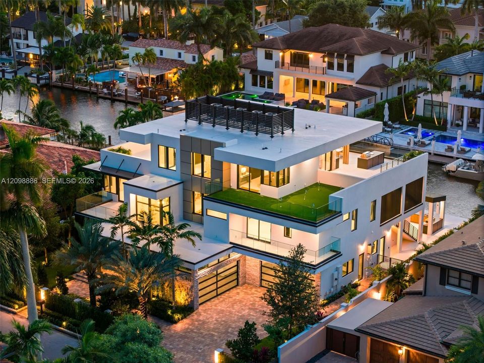 Modern multi-level estate featuring expansive flat-roof terraces, artificial turf accents, floor-to-ceiling glass paneling, a paved driveway, and private canal frontage