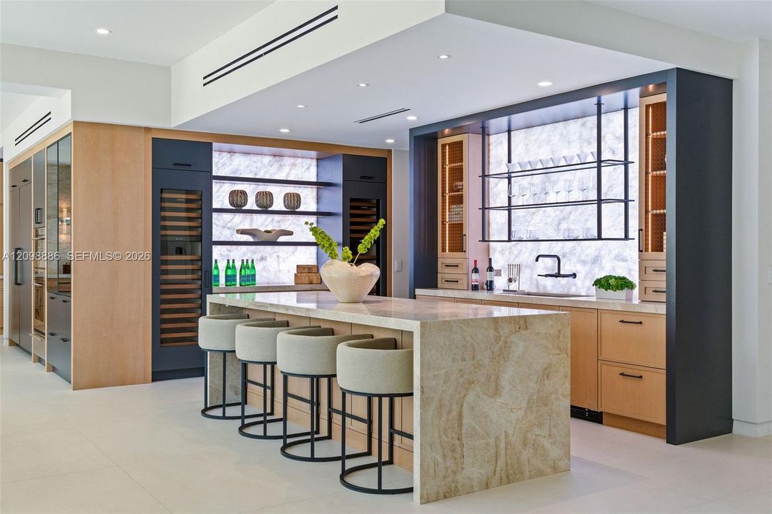Kitchen featuring a waterfall-edge stone island, built-in dual wine refrigeration, stone slab backsplash, recessed ceiling lighting, and custom cabinetry with open metal shelving