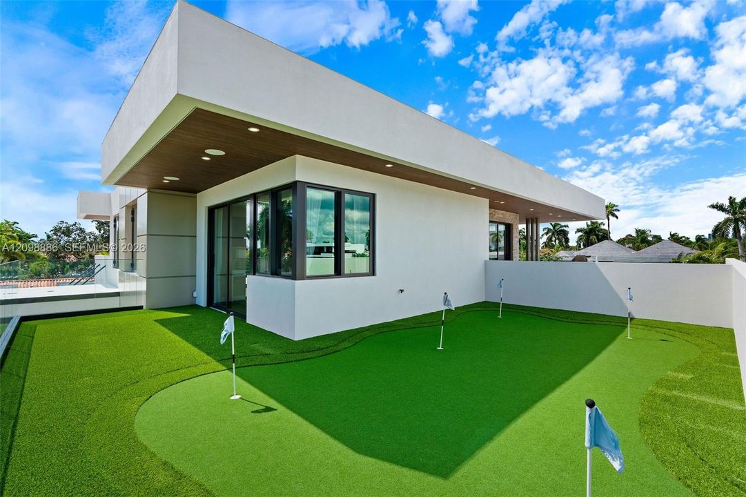 Contemporary rooftop terrace featuring a multi-hole putting green, synthetic turf surfacing, flat-roof architecture, recessed ceiling lighting, and floor-to-ceiling glass windows