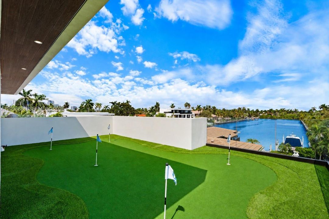 Rooftop putting green with synthetic turf, perimeter walls, and recessed ceiling lighting, overlooking water