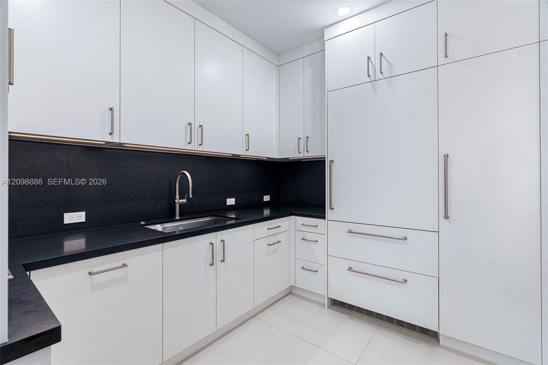 Kitchen featuring flat-panel white cabinetry, contrasting dark stone countertops, integrated panel-ready refrigerator, stainless steel undermount sink with gooseneck faucet, and recessed ceiling lighting