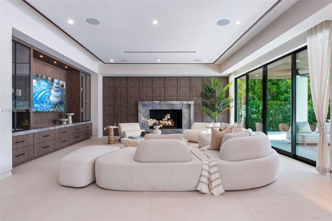 Living area featuring custom wood-finish built-in cabinetry, stone-surround fireplace, dark wood paneled accent wall, recessed ceiling lighting, and floor-to-ceiling sliding glass doors