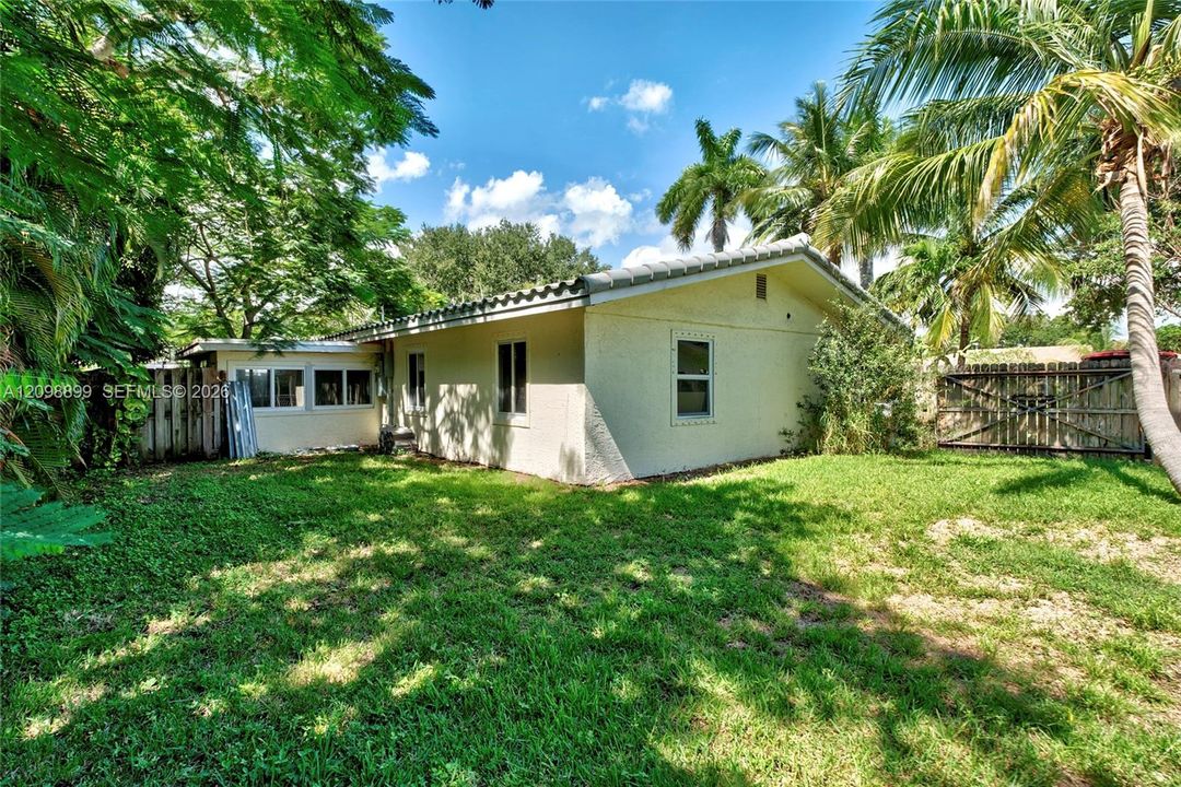 Stucco exterior residence featuring a tiled roof, expansive lawn, mature perimeter trees, and a wooden privacy fence