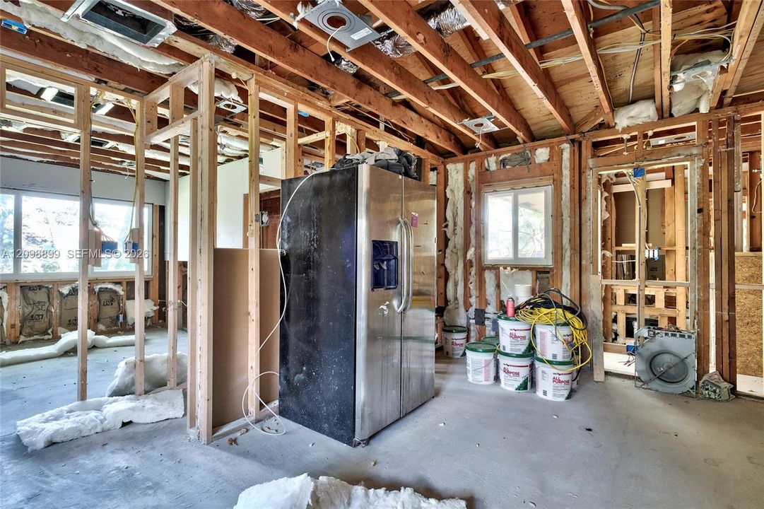 Interior space featuring exposed wood framing, concrete flooring, stainless steel side-by-side refrigerator, multi-pane windows, and thermal insulation