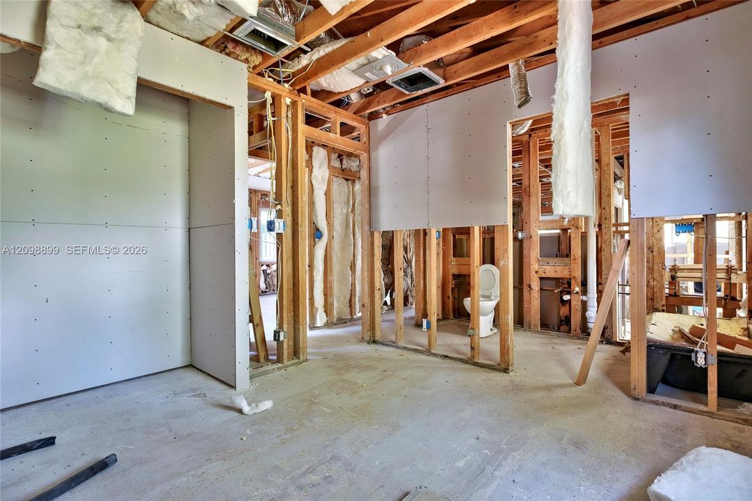Interior structure featuring exposed wood framing, installed drywall panels, concrete flooring, and an in-place toilet fixture