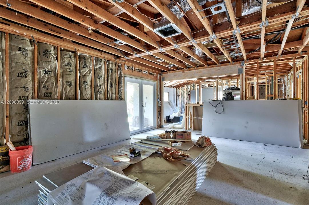 Structural interior space featuring exposed wood framing, installed fiberglass batt insulation, and dual-pane glass entry doors