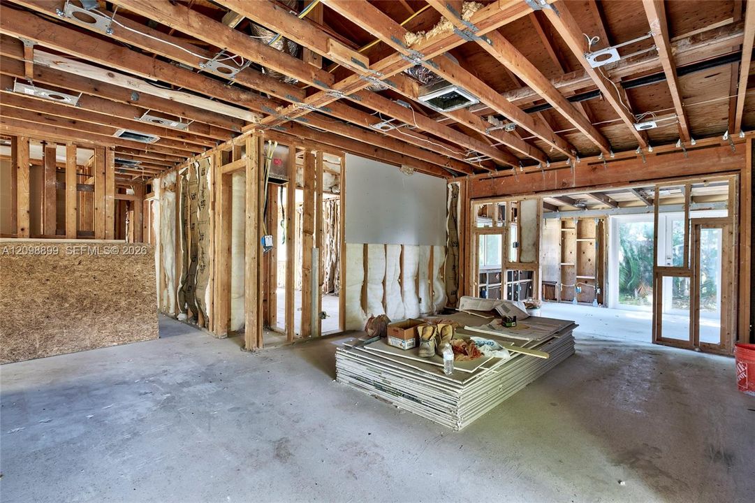 Open-concept interior featuring exposed wood-stud framing, visible ceiling joists, concrete flooring, and large structural openings