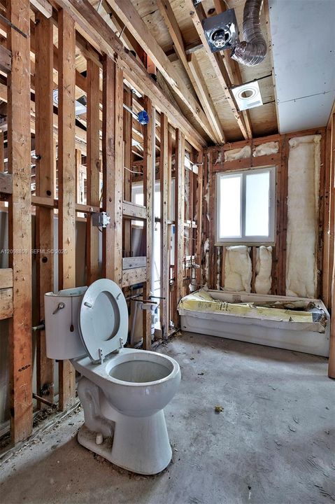 Interior space featuring exposed wood framing, concrete flooring, a white bathtub, a single-flush toilet, and a window